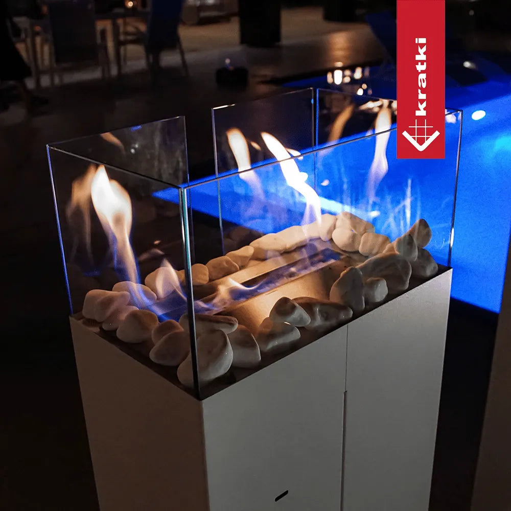 Kratki Romeo TÜV haard met glazen ombouw en decoratieve stenen, brandend in een moderne omgeving.