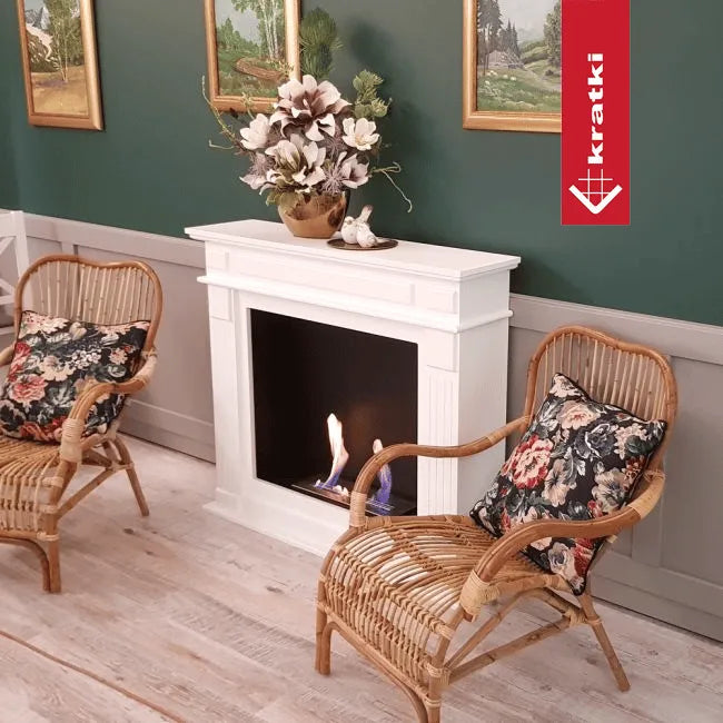 Gezellige woonkamer met Kratki November haard, rotan stoelen en bloemen op de schouw.