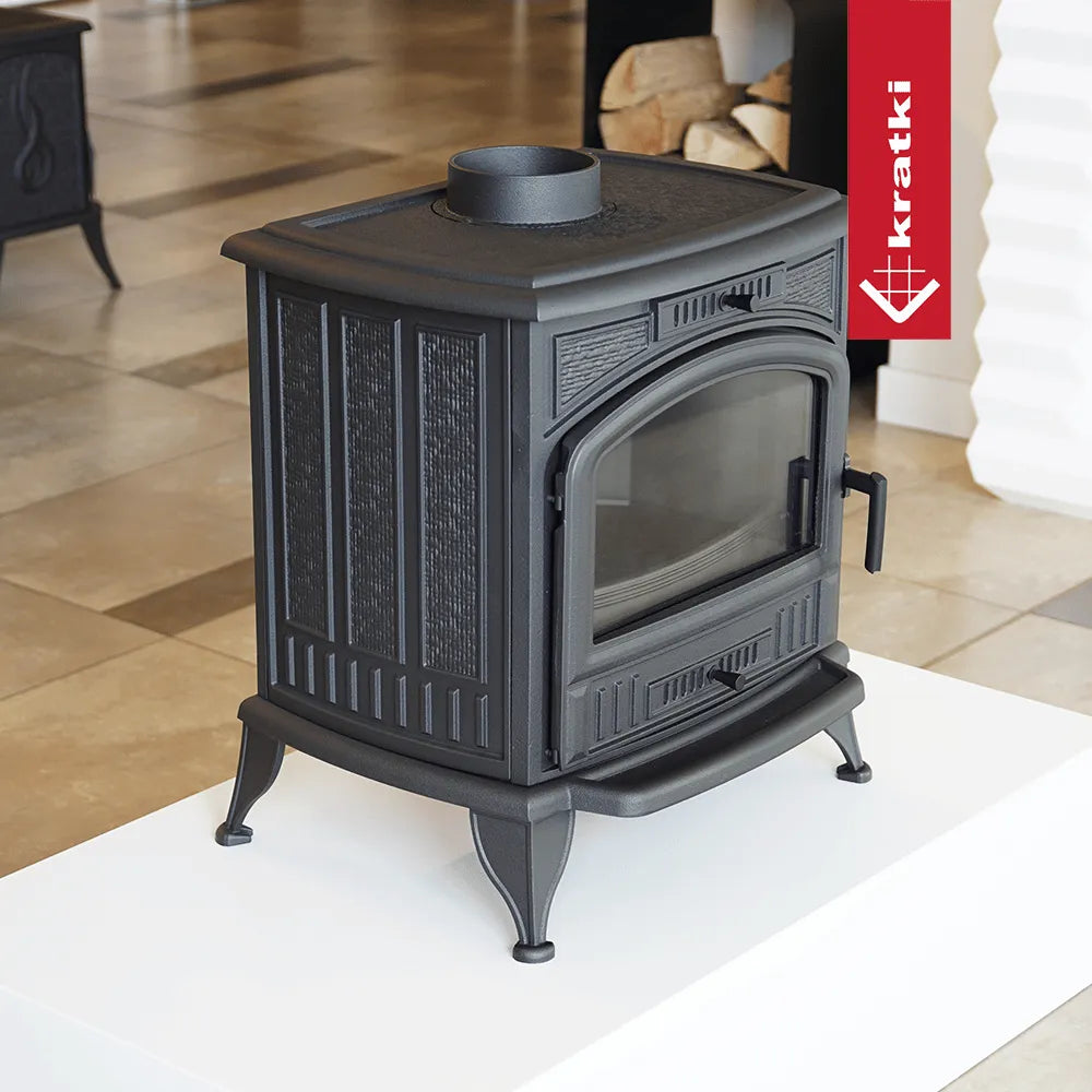 Zwarte gietijzeren houtkachel Kratki K6 met glazen deur en decoratieve panelen.
