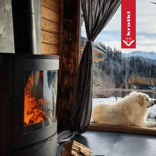 Kratki AB 2 houtkachel in een gezellige chalet met uitzicht op besneeuwde bergen en een hond.