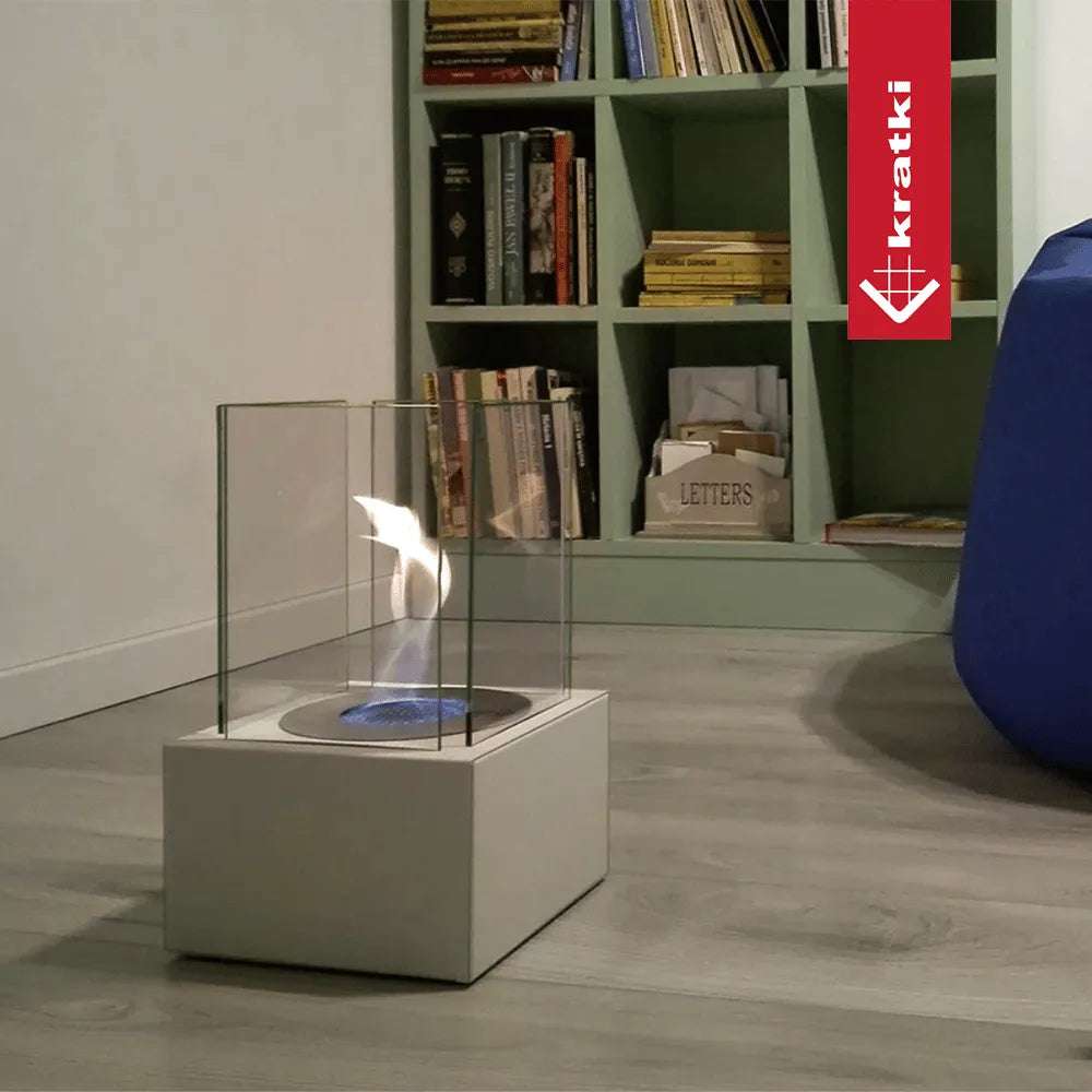Kratki Tango1 bio-ethanol haard in moderne woonkamer met boekenplank en blauwe stoel.