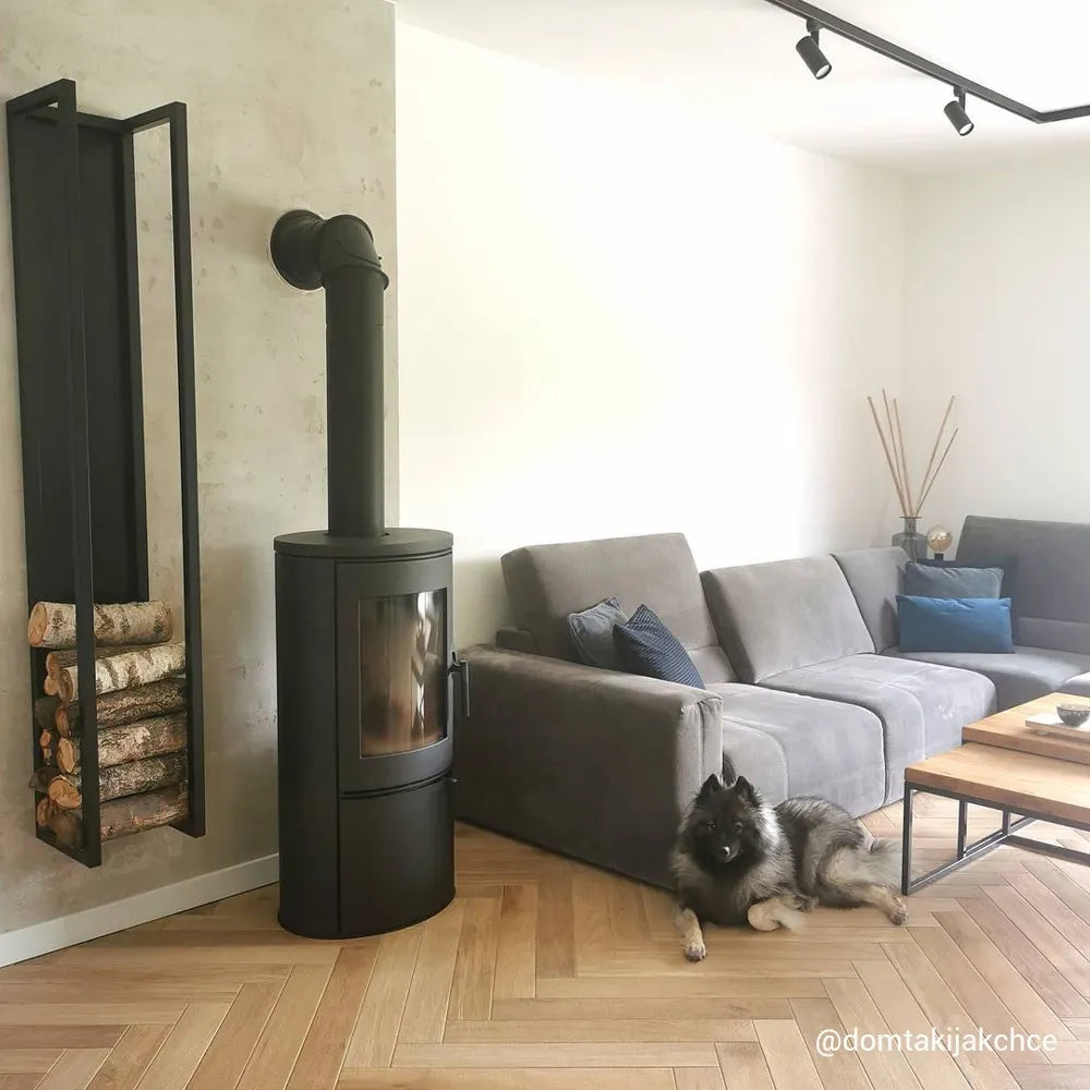 Kratki AB houtkachel in moderne woonkamer met grijze bank en hond op houten vloer.