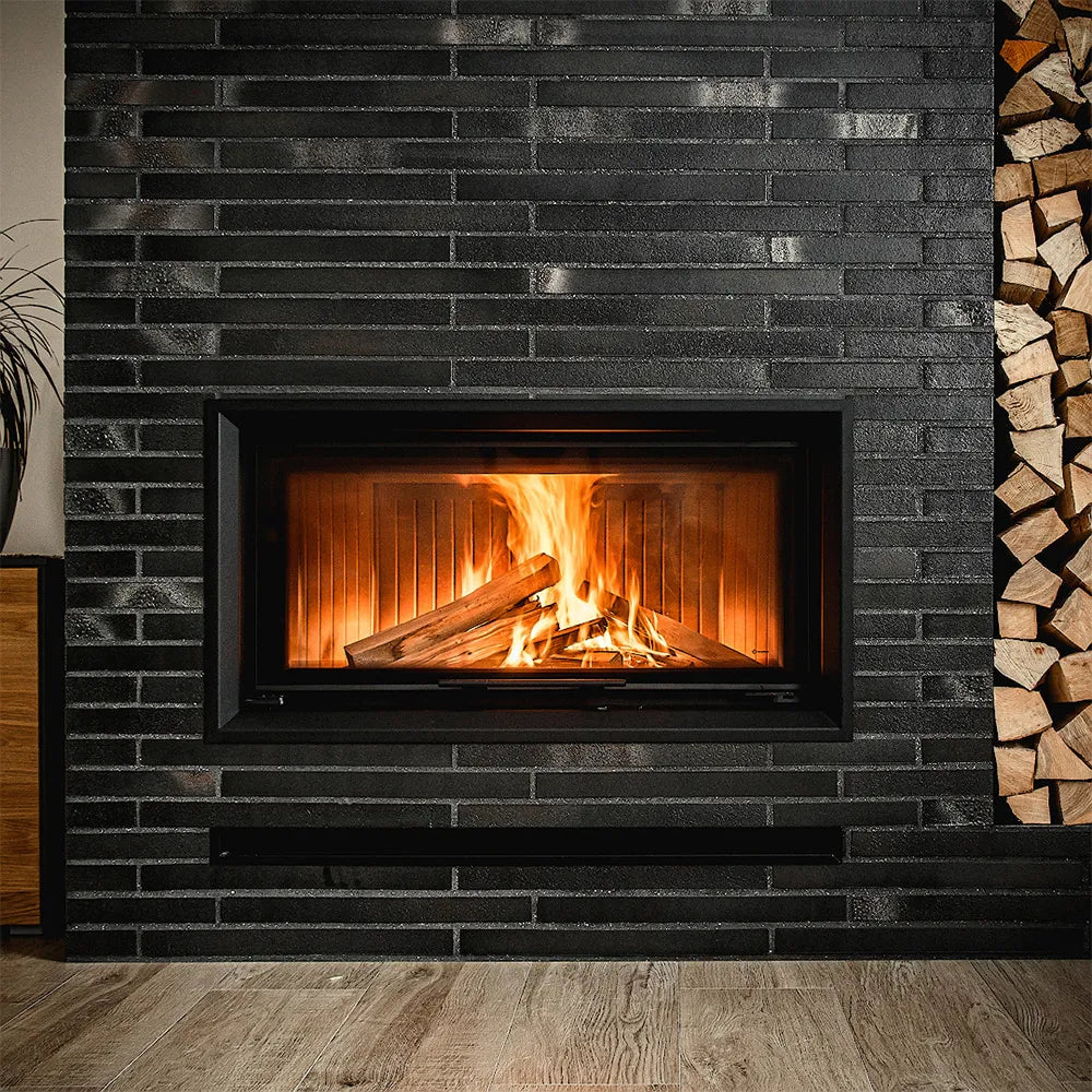 Kratki Nadia 14 kW ingebouwd in een moderne, zwarte bakstenen muur met brandend hout.