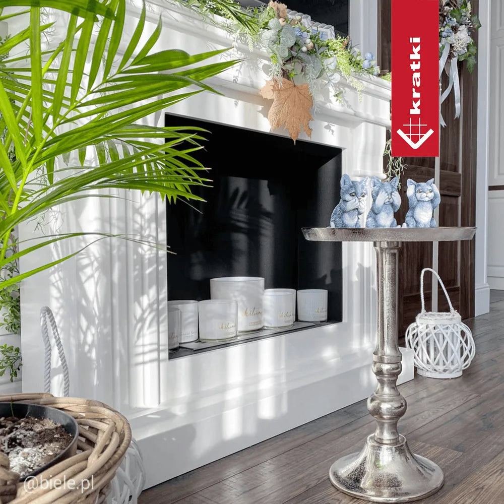 Witte schouw met Kratki August TÜV, versierd met kaarsen en planten, naast een zilveren bijzettafel.
