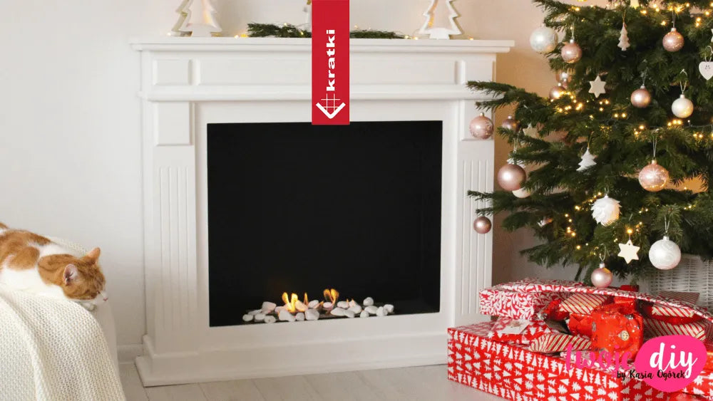 Kratki November TÜV haard naast versierde kerstboom en slapende kat op deken.