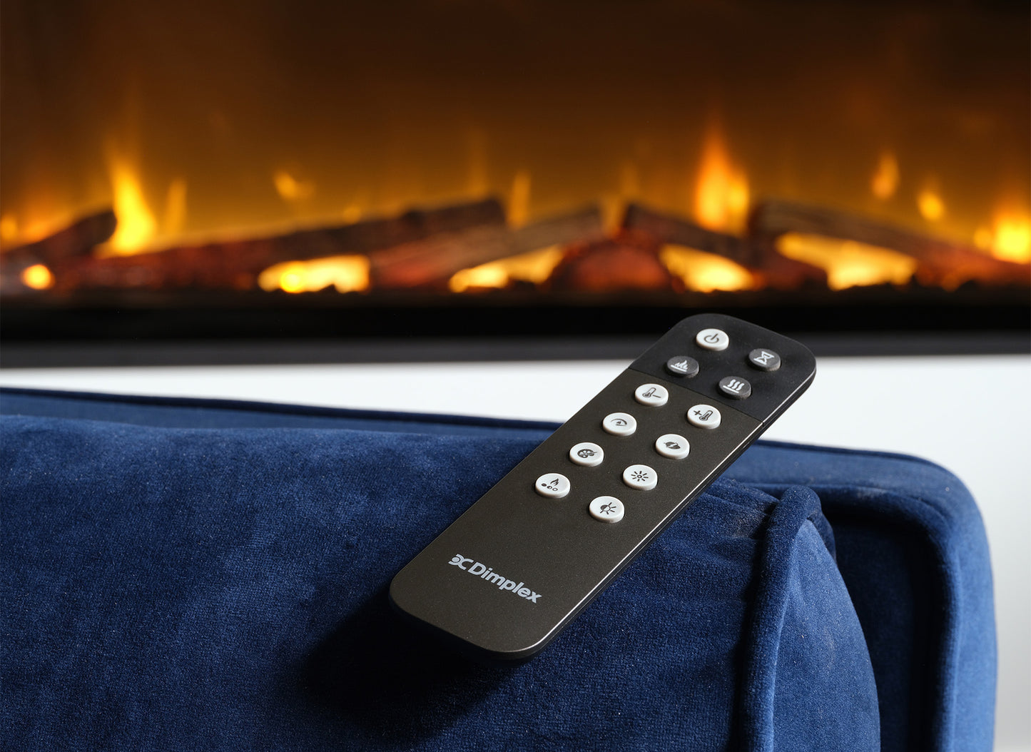 Dimplex Ignite Evolve 74 met afstandsbediening op een blauwe bank, vlammen op de achtergrond.