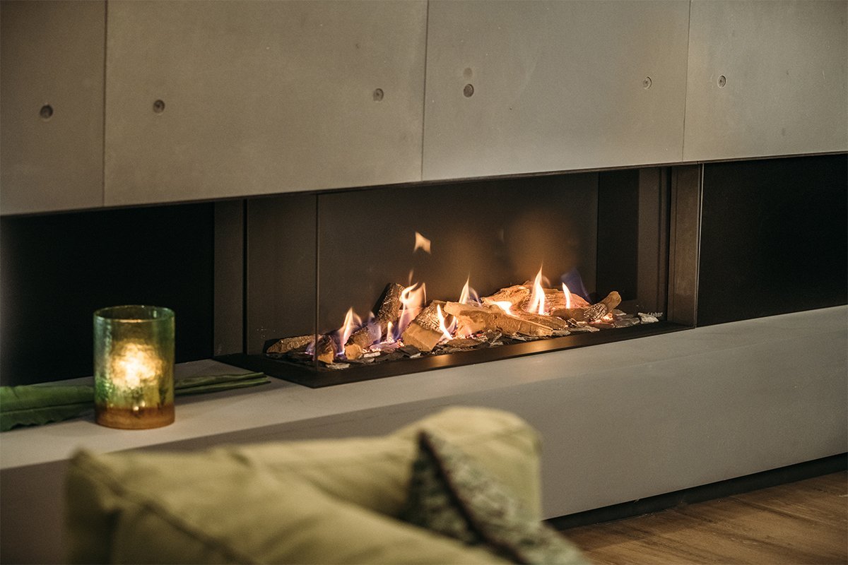 Faber MatriX 1050/400 II Hoek, moderne hoekhaard met brandende houtblokken en een groene kaars.