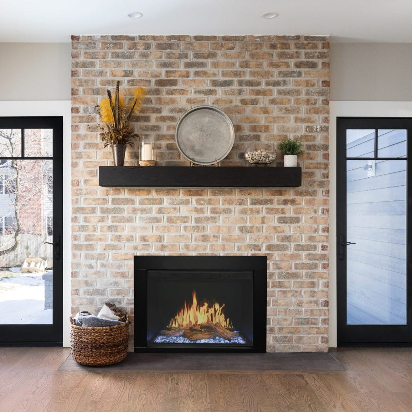 Bakstenen muur met Wanders Orion Traditional 26'' haard, zwarte plank en decoratieve objecten erboven.