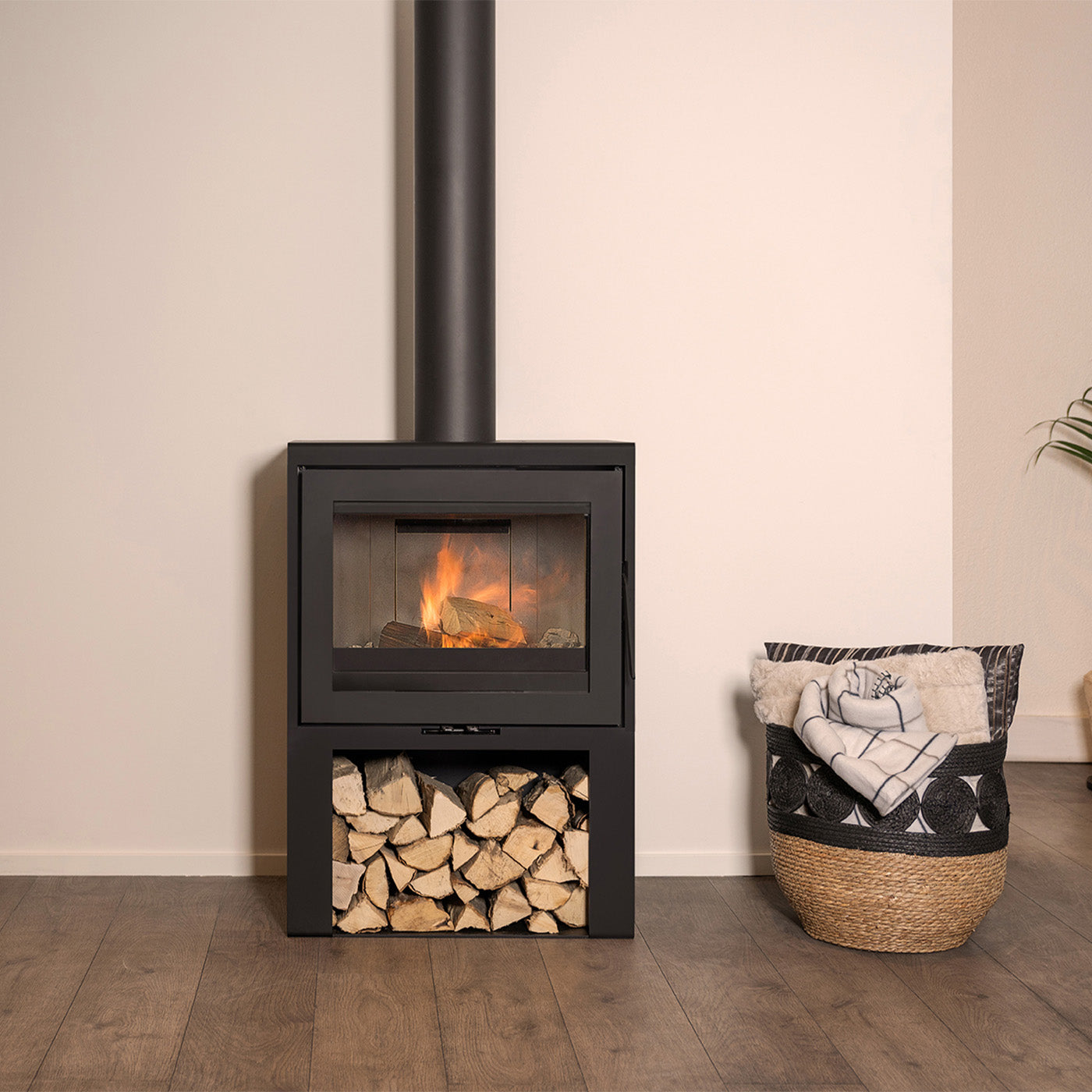 Wanders WAN-2075 Black Edition High, een moderne houtkachel met brandend vuur en houtopslag eronder.
