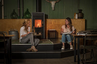 Wanders Pecan Eco Medium speksteenkachel brandt in sfeervolle ruimte met twee zittende vrouwen