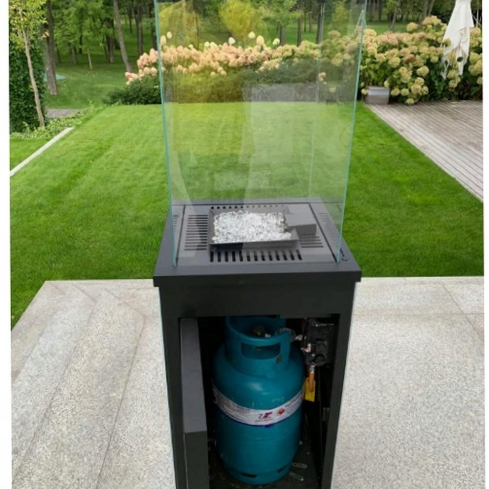 Krátki Patio terrasvuurtafel met glazen windscherm en zichtbare gasfles in een tuin