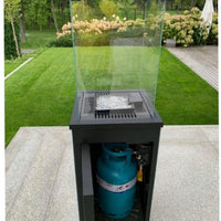 Krátki Patio terrasvuurtafel met glazen windscherm en zichtbare gasfles in een tuin