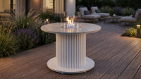 Balstil Table Core vuurtafel met vlam, glazen windscherm en ronde tafelbladen op een terras.