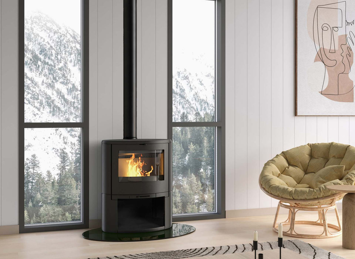 Dovre BOW/WB houtkachel met brandend vuur in een modern interieur met fauteuil en bosuitzicht.