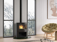 Dovre BOW/WB houtkachel met brandend vuur in een modern interieur met fauteuil en bosuitzicht.