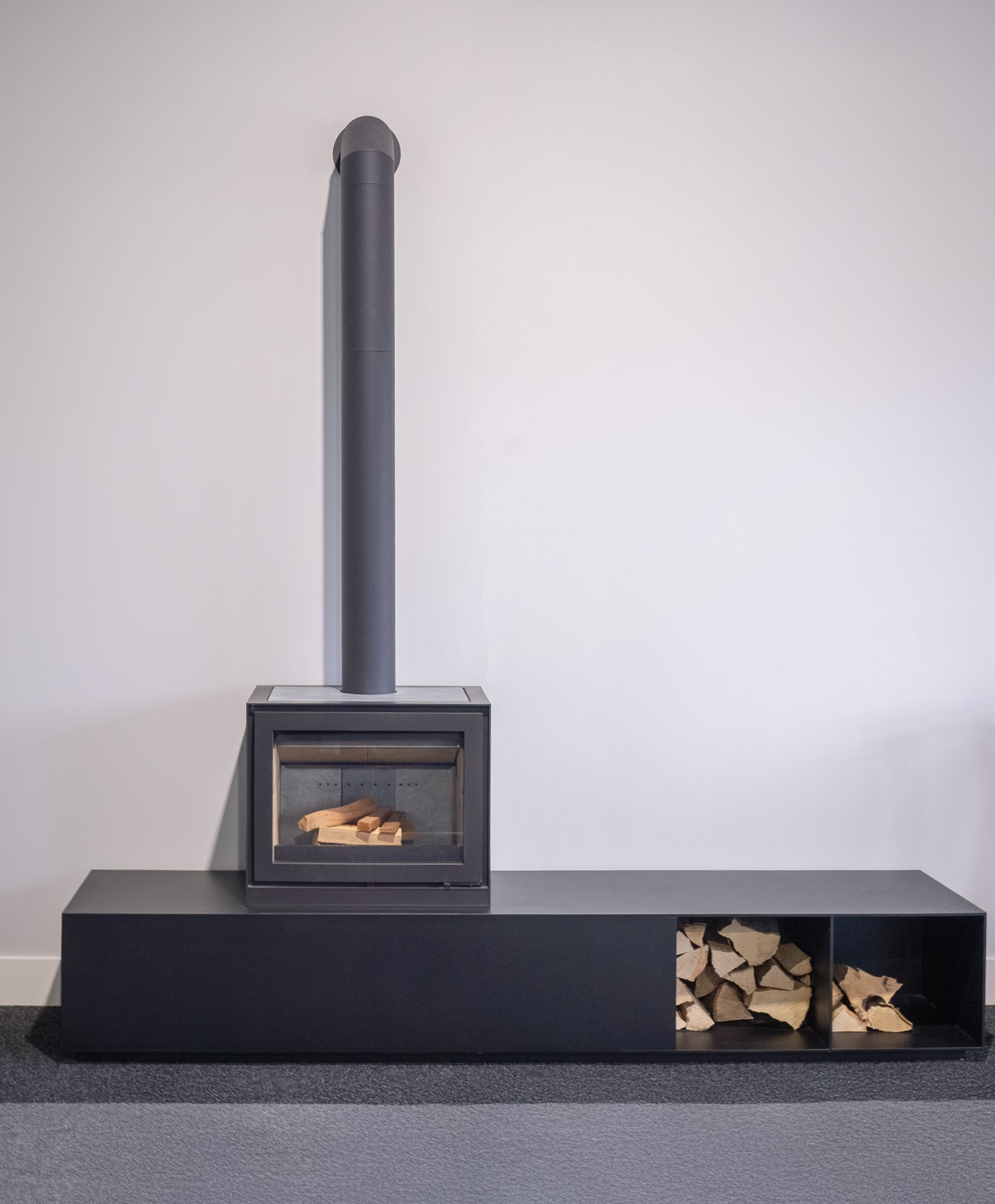 Altech MAX W houtkachel op zwarte sokkel met houtopslag
