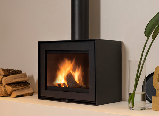 Wanders WAN-2060 Black Edition Low houtkachel met brandend vuur, naast houtblokken en een vaas.