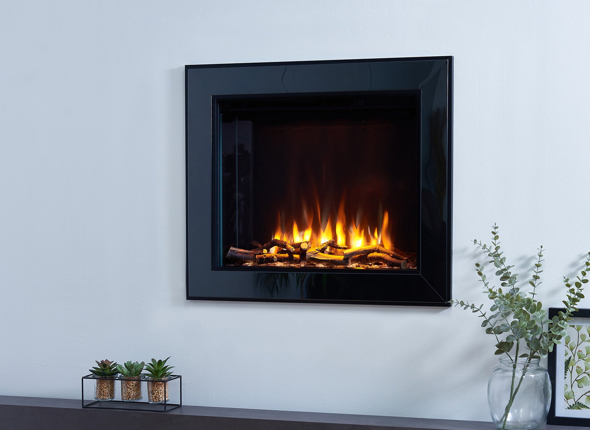 Charlton & Jenrick i-560e Slim elektrische haard met brandende houtblokken en decoratieve planten.