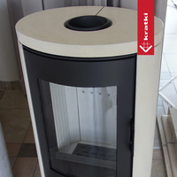 Kratki AB DR-kachel met ronde lichte bovenplaat en donkere glazen deur in een interieur.