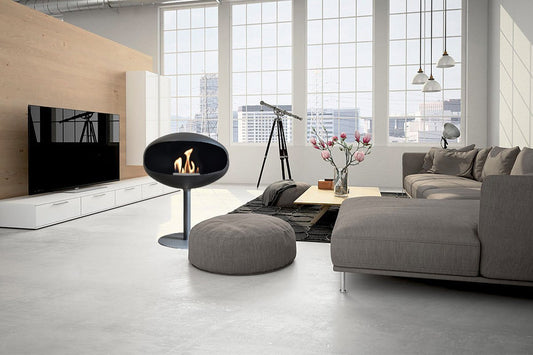 Cocoon Fires Pedestal (Zwart) in een moderne woonkamer met grote ramen en grijze meubels.