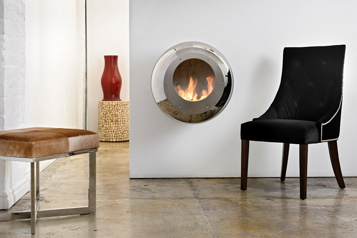 Cocoon Fires Vellum (RVS) wandhaard in minimalistische ruimte met stoel en poef