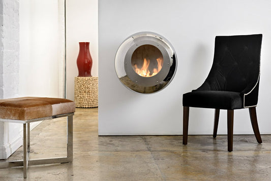 Cocoon Fires Vellum (RVS) ronde wandhaard in moderne kamer met zwarte stoel en bruine poef.