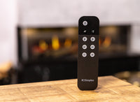 Dimplex Opti-V Vista 130 I afstandsbediening op houten tafel, haard op achtergrond